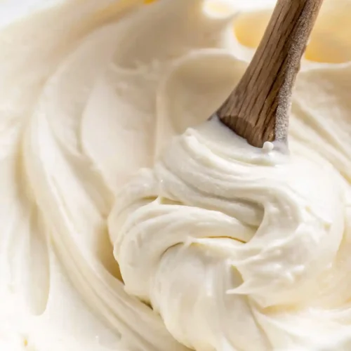 Smooth vanilla buttercream frosting being stirred with a wooden spoon in a glass bowl