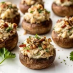 Close-up of a vegetarian stuffed mushroom topped with creamy filling, chopped nuts, and fresh parsley on a white plate.
