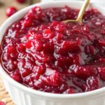 Close-up of thick homemade cranberry sauce in a white bowl with a gold spoon, perfect for holiday meals.