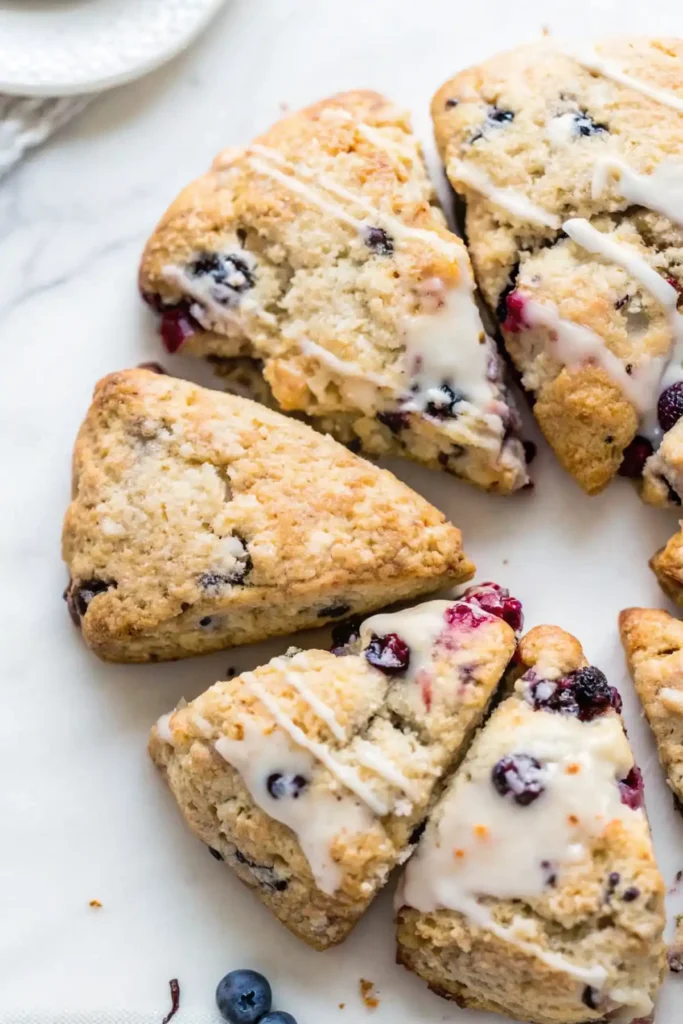Flaky glazed scones with blueberries and cranberries on marble surface
