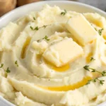 Creamy homemade mashed potatoes in a white bowl topped with melting butter and fresh thyme sprigs