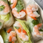 Close-up of Vietnamese shrimp spring rolls wrapped in rice paper with lettuce, herbs, and sliced chili.