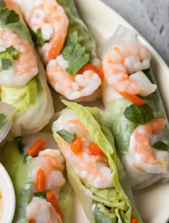 Close-up of Vietnamese shrimp spring rolls wrapped in rice paper with lettuce, herbs, and sliced chili.