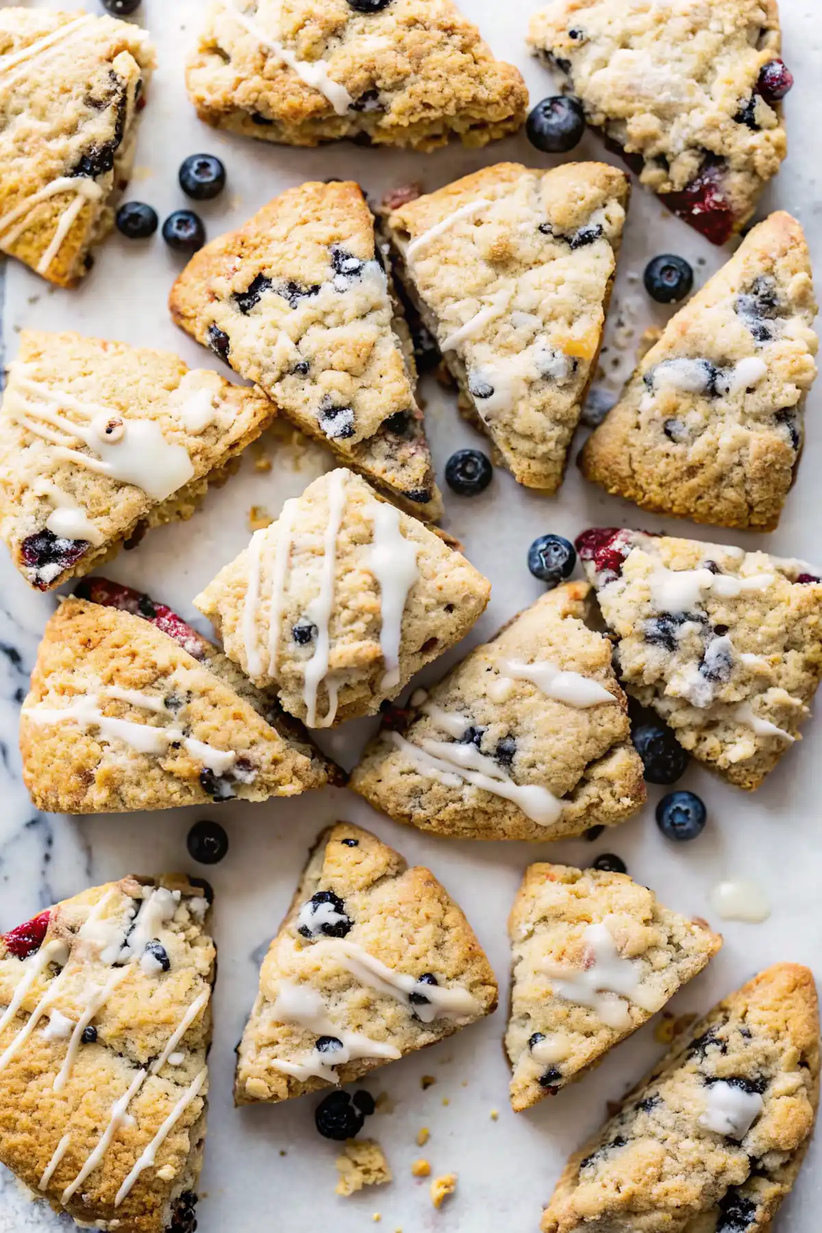 Freshly baked blueberry scones with icing drizzle on marble surface