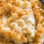 Close up of creamy baked macaroni and cheese with golden crispy breadcrumb topping and a spoon scooping rich cheese covered elbow pasta.