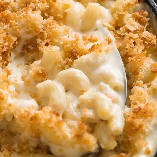 Close up of creamy baked macaroni and cheese with golden crispy breadcrumb topping and a spoon scooping rich cheese covered elbow pasta.