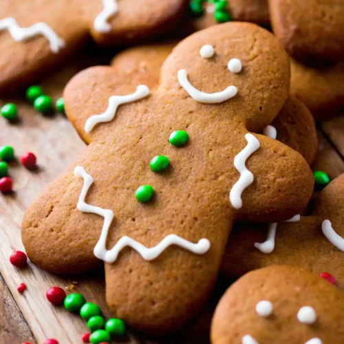 Chewy gingerbread men cookies with white icing smiles and green candy buttons on a rustic wooden table.