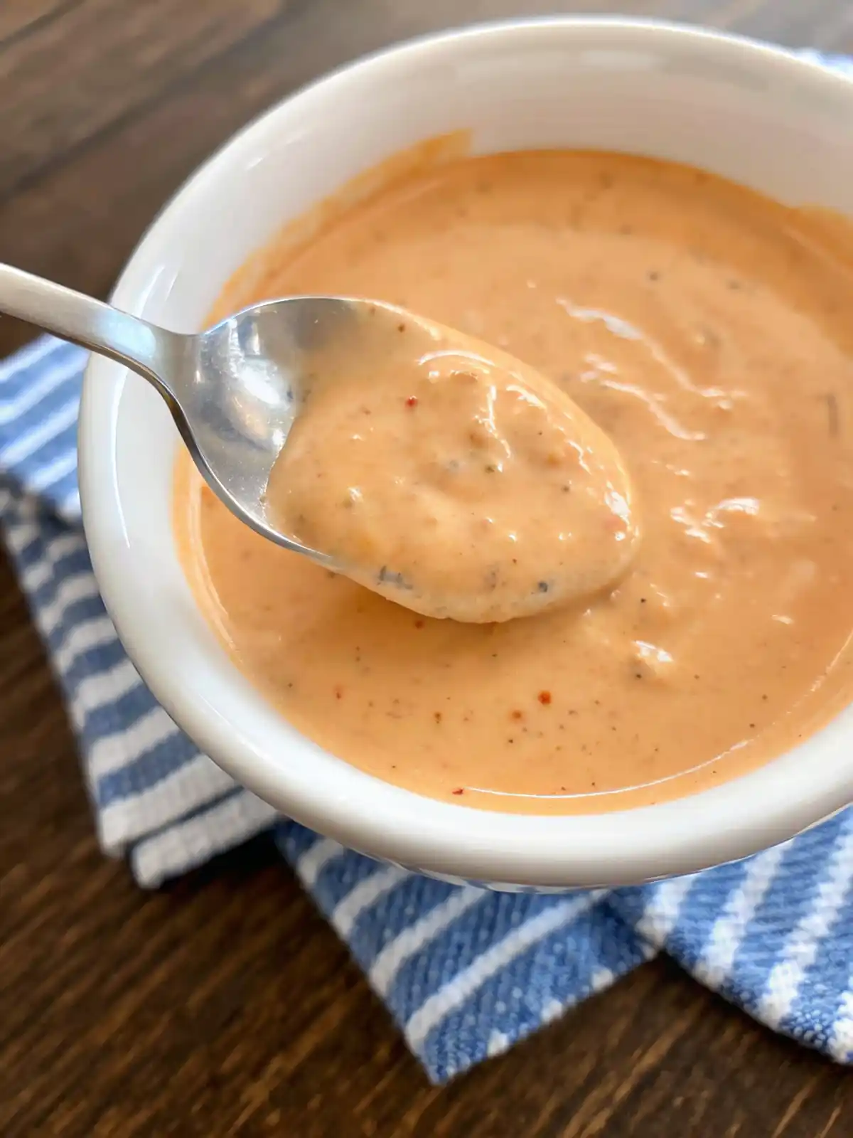 Close up of homemade Big Mac sauce in a white bowl with a spoon showing thick creamy texture and paprika specks.