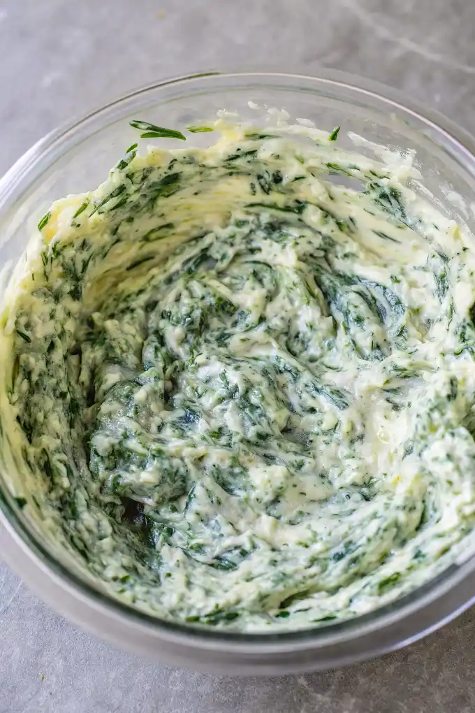 Creamy spinach dip mixture in a clear glass bowl ready to be baked