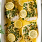 Garlic butter baked cod fillets with lemon slices and fresh parsley in a white baking dish.