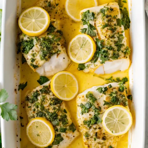 Garlic butter baked cod fillets with lemon slices and fresh parsley in a white baking dish.