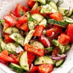 Healthy cucumber tomato salad with fresh dill, red onion, olive oil, and cracked black pepper in a white bowl.