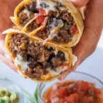 Beef burrito cut in half showing seasoned ground beef, black beans, melted cheese, and diced tomatoes, served with salsa and guacamole.