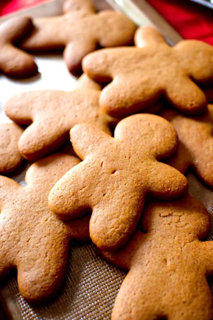 No spread gingerbread cookies cooling on a baking sheet with golden brown edges and smooth tops.