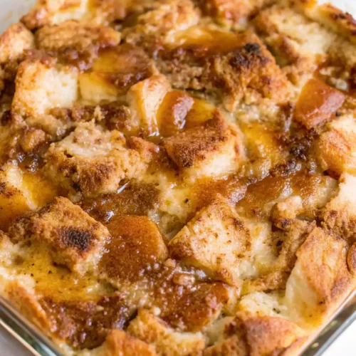Freshly baked old fashioned bread pudding in a glass dish with a golden brown top and caramelized cinnamon sugar crust.