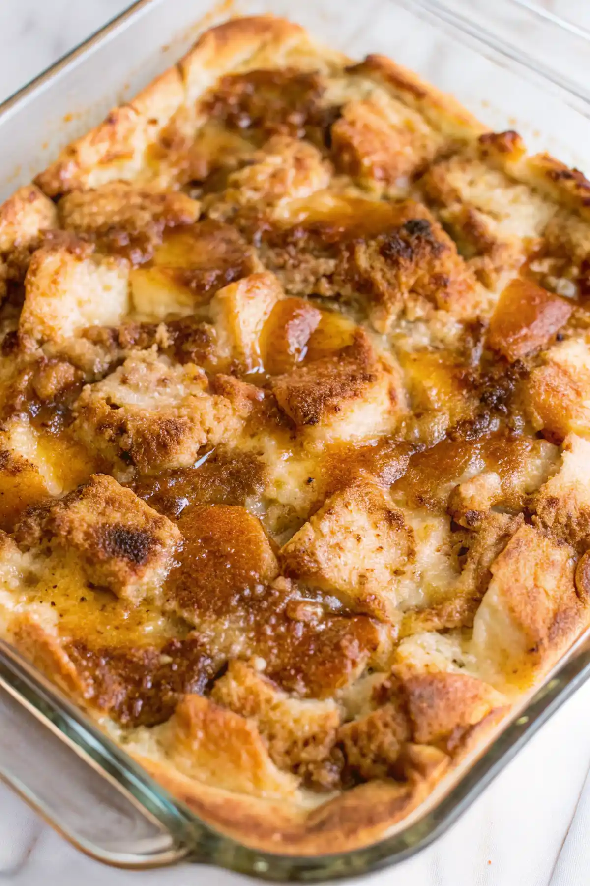 Freshly baked old fashioned bread pudding in a glass dish with a golden brown top and caramelized cinnamon sugar crust.