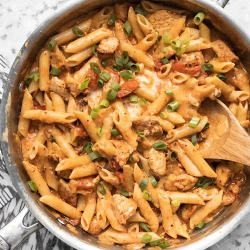 One pot creamy Cajun chicken pasta with penne, seared chicken pieces, fire roasted tomatoes, and fresh green onions in a skillet.