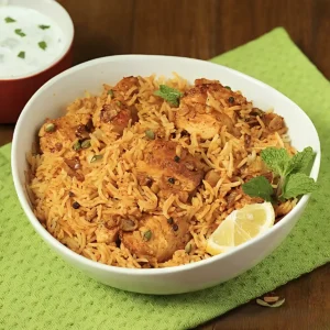 Restaurant Style Chicken Biryani served in a white bowl with fluffy basmati rice, tender chicken pieces, mint garnish, lemon wedge, and raita on the side.