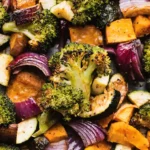 Close up of oven roasted vegetables with broccoli, sweet potatoes, zucchini, and red onions caramelized on a sheet pan
