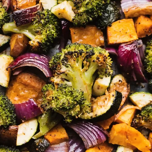 Close up of oven roasted vegetables with broccoli, sweet potatoes, zucchini, and red onions caramelized on a sheet pan