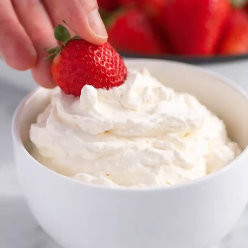 Hand placing fresh strawberry on homemade whipped cream in white bowl
