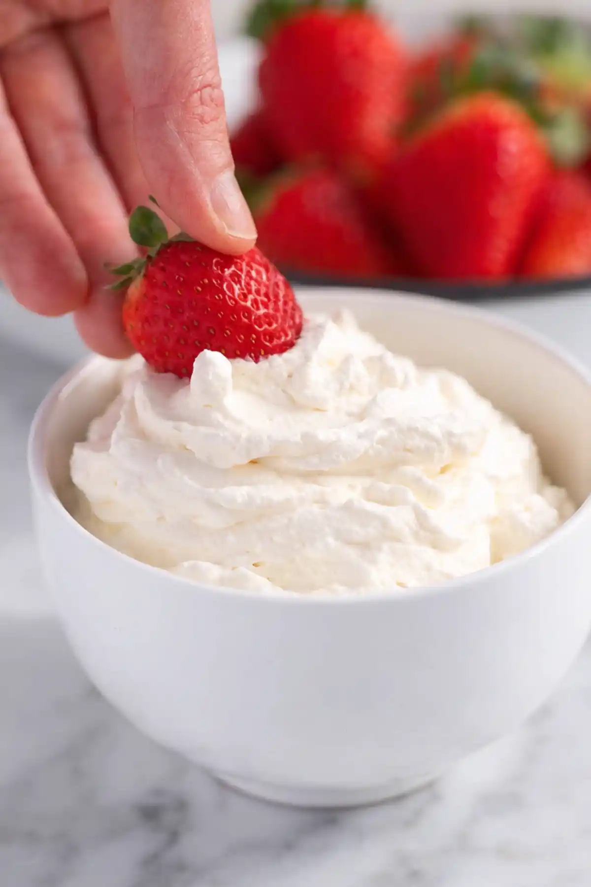 Hand placing fresh strawberry on homemade whipped cream in white bowl