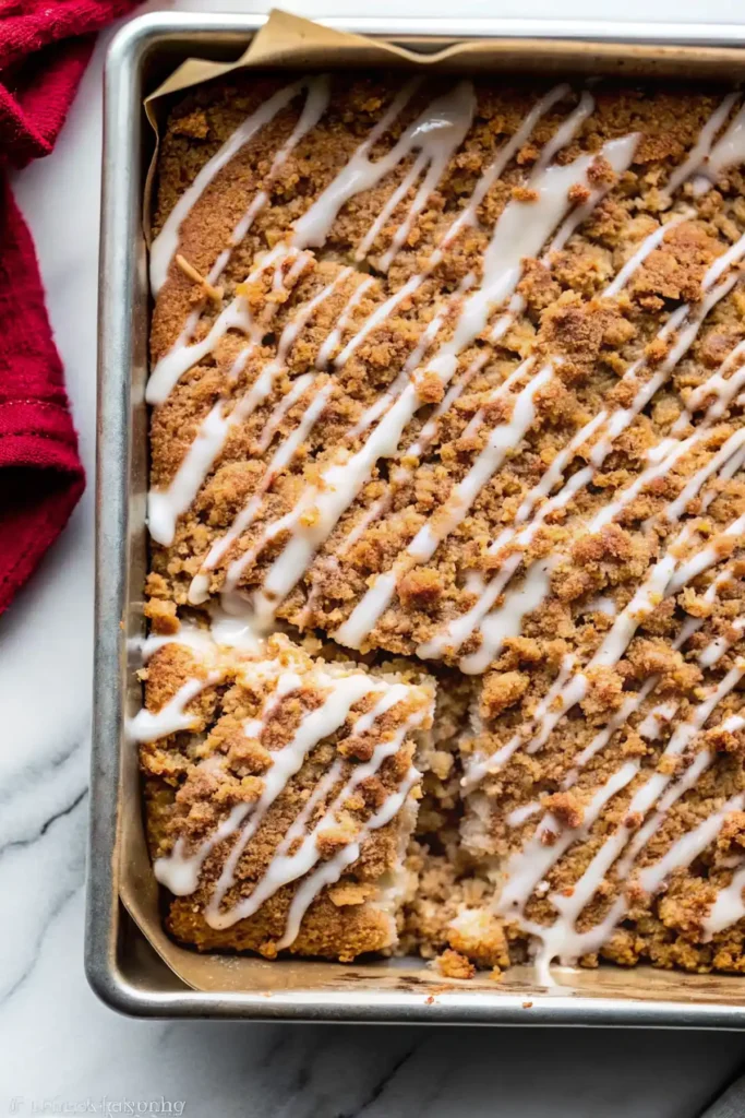 Sour cream coffee cake in a pan with crumb topping and icing drizzle