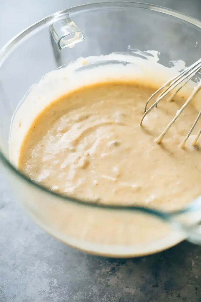 Banana cake batter in glass mixing bowl with whisk