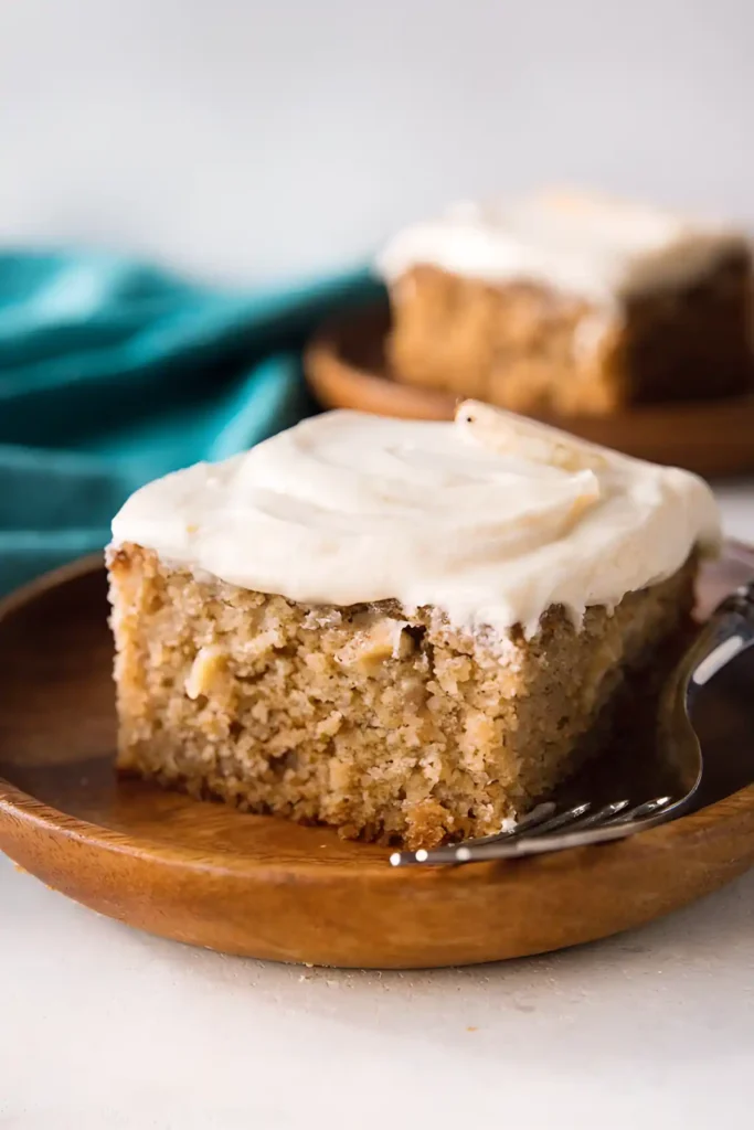 Best banana cake recipe slice with cream cheese frosting on wooden plate