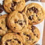 Chewy brown butter chocolate chip cookies with melted chocolate chunks on parchment paper over a rustic tray.