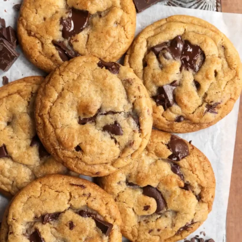 Chewy brown butter chocolate chip cookies with melted chocolate chunks on parchment paper over a rustic tray.