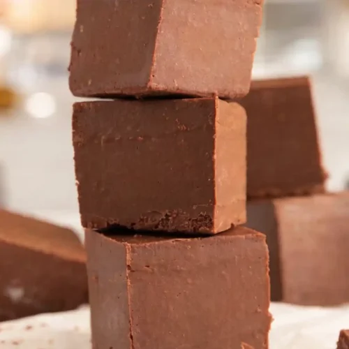 Stacked chocolate fudge cubes made with condensed milk on parchment paper, showing smooth creamy texture and rich chocolate color.