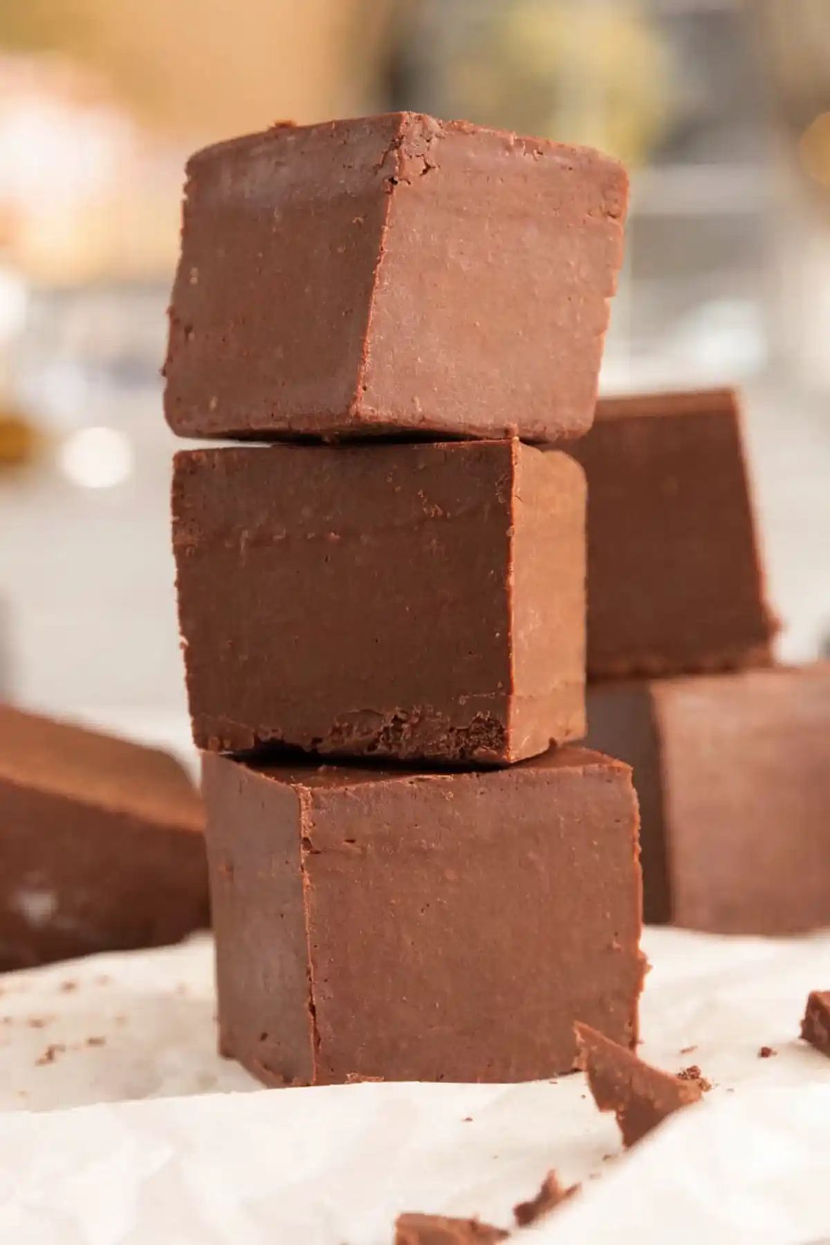 Stacked chocolate fudge cubes made with condensed milk on parchment paper, showing smooth creamy texture and rich chocolate color.