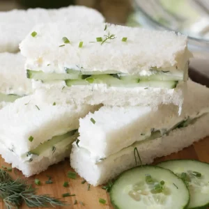 Cream cheese cucumber sandwiches made with thin cucumber slices and herb spread on soft crustless white bread, cut into small tea sandwich pieces.