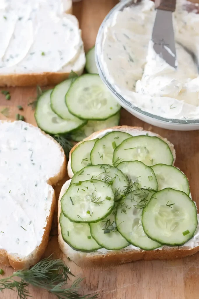 Open faced cucumber sandwich with thin cucumber slices and creamy herb cream cheese spread on soft white bread.
