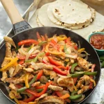 Chicken fajitas in a skillet with bell peppers and onions served with warm tortillas and salsa