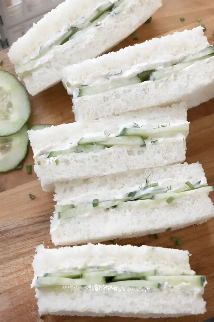 English cucumber finger sandwiches with creamy herb spread on soft crustless white bread arranged on a wooden board.