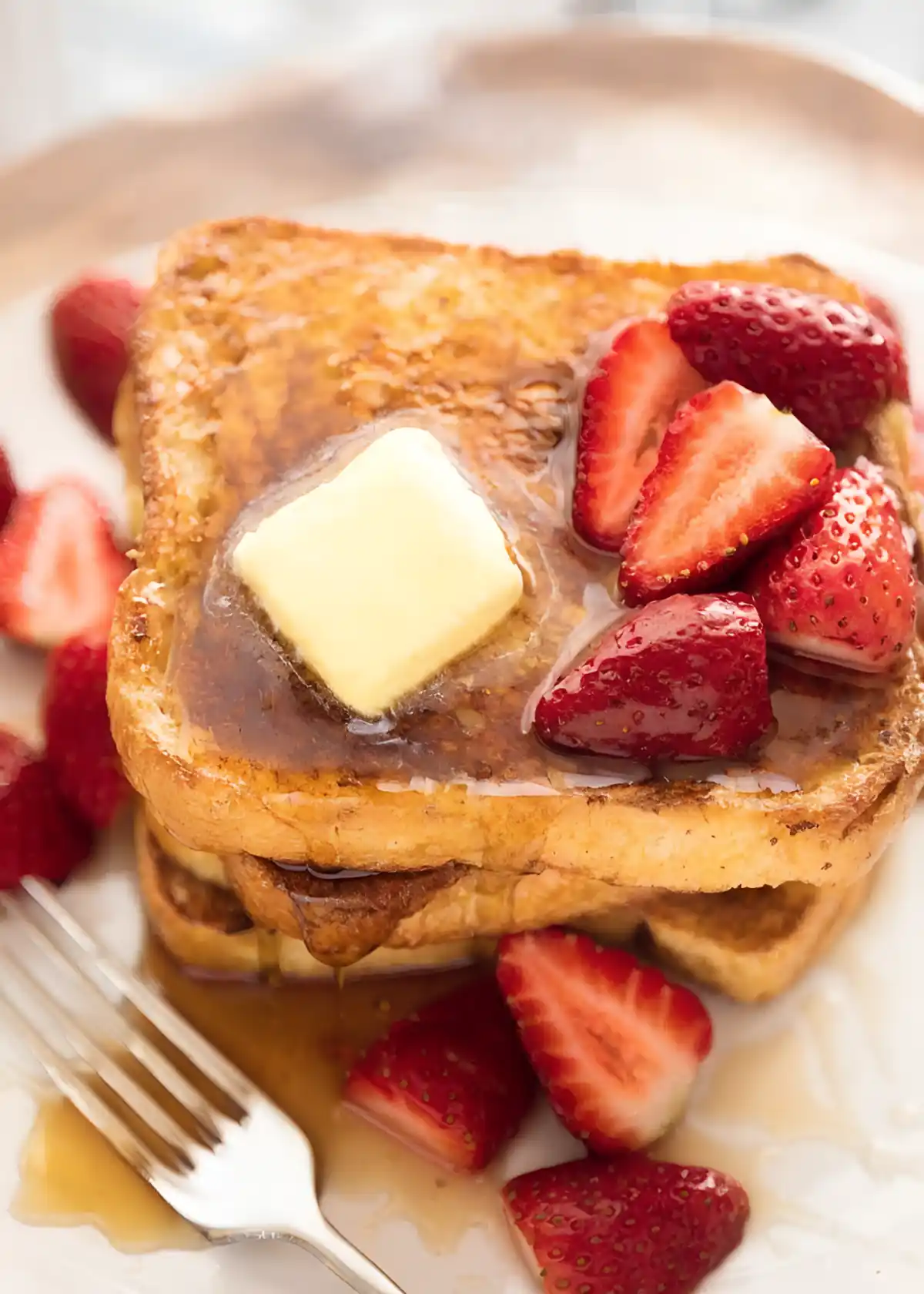 French toast topped with melting butter, maple syrup, and fresh strawberries on a white plate.