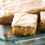 Moist banana cake square with cream cheese frosting in a glass baking dish