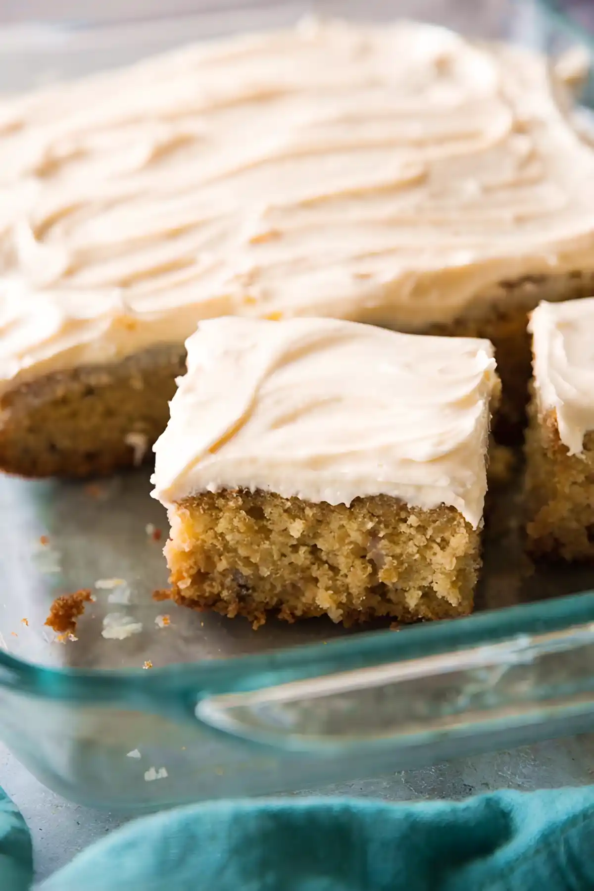 Moist banana cake square with cream cheese frosting in a glass baking dish