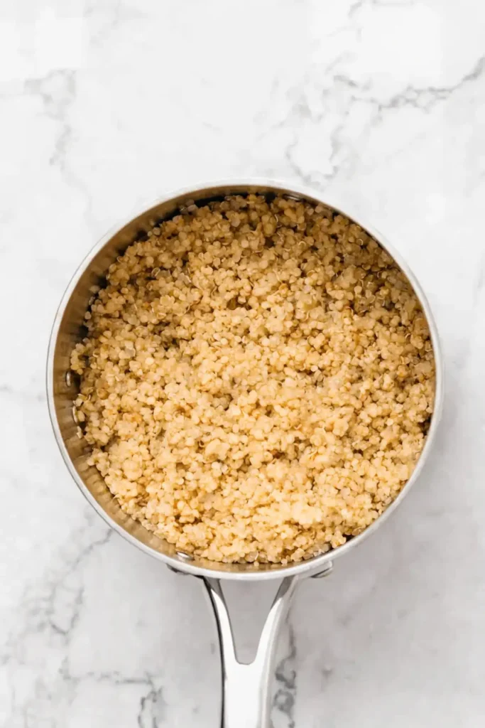 Top view of fluffy cooked quinoa in a stainless steel saucepan on a white marble countertop.
