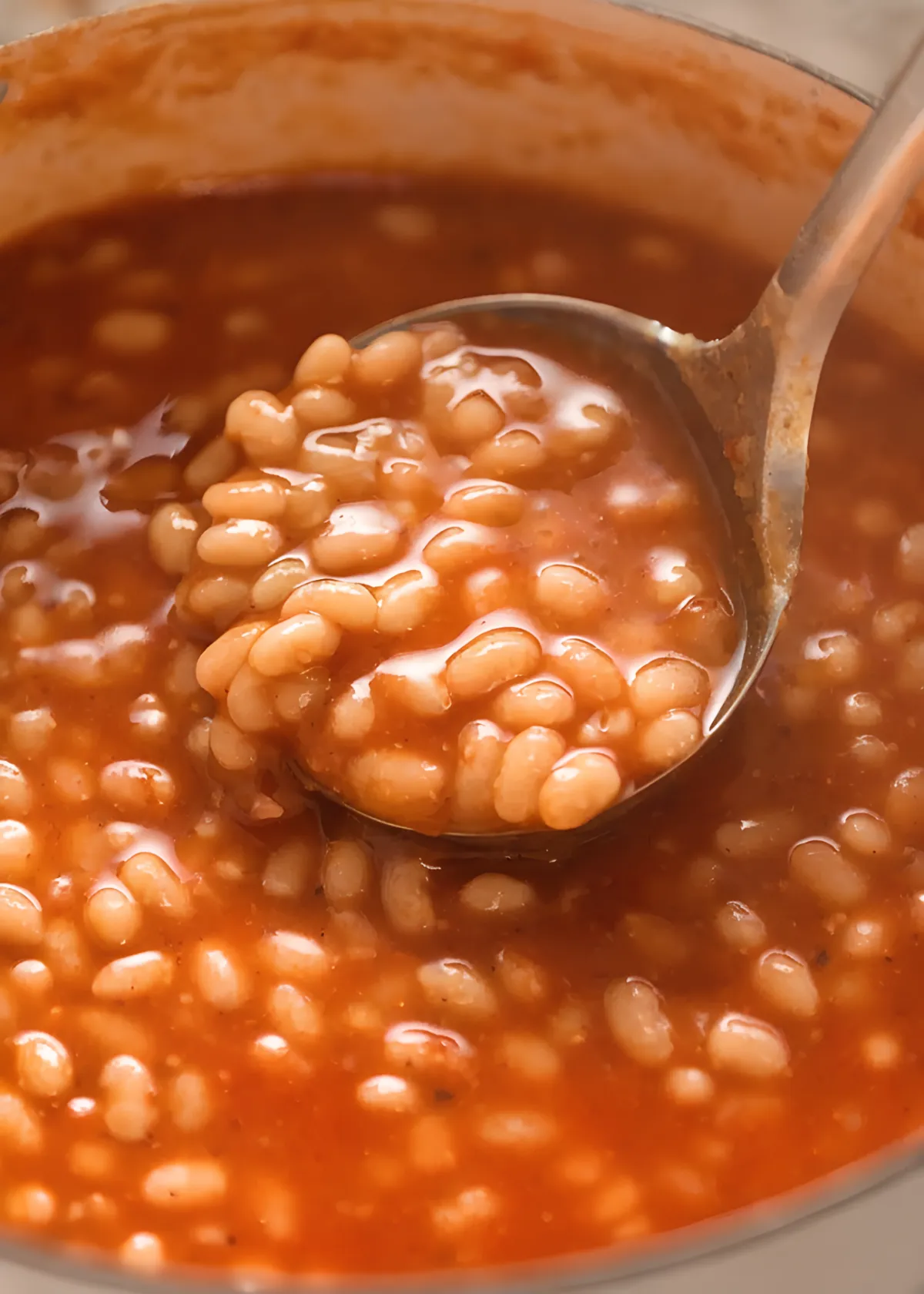 Homemade baked beans in rich tomato sauce with a spoon scooping soft white beans