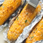 Baked corn on the cob wrapped in foil brushed with garlic butter