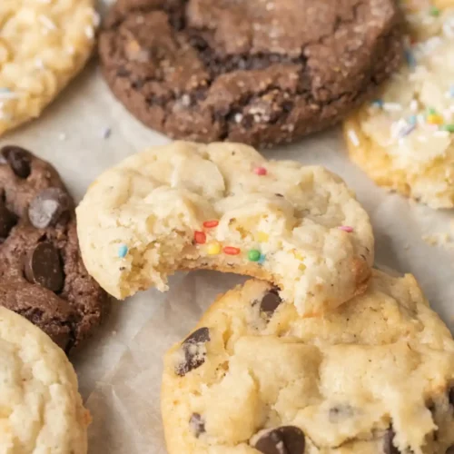 Soft cake mix cookies with chocolate chips and funfetti sprinkles on parchment paper, including a broken cookie showing a chewy center.