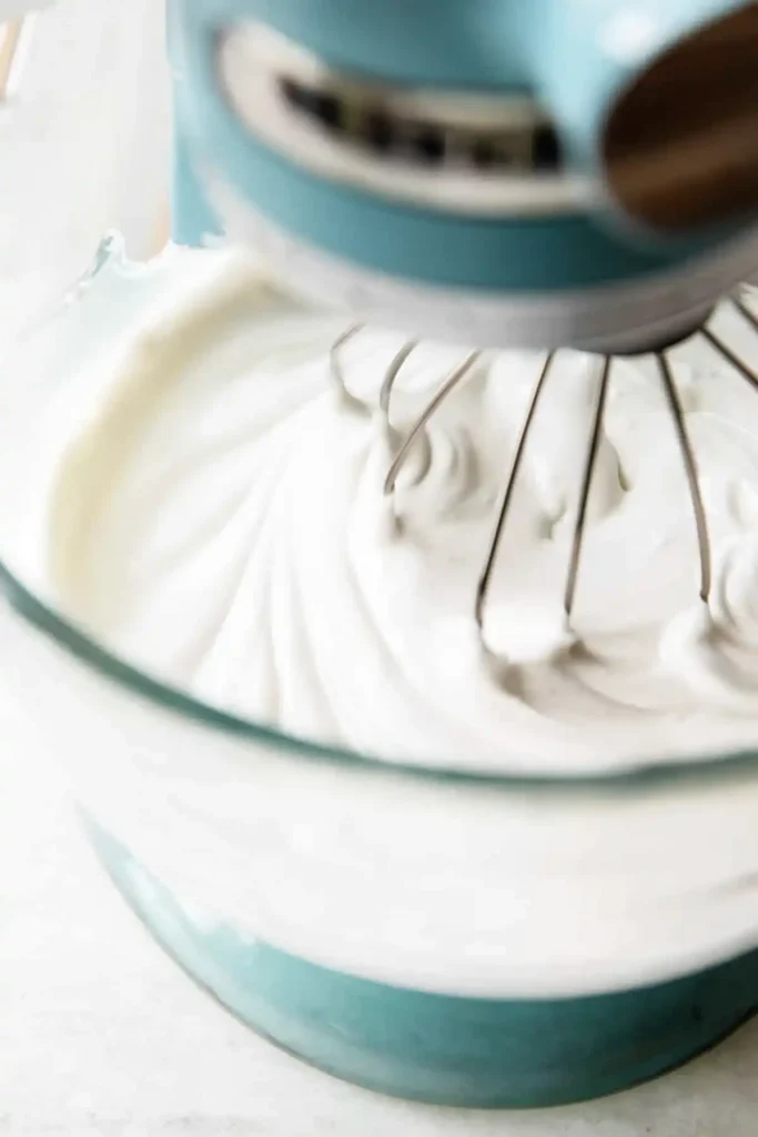 Royal icing being whipped in a bowl with electric mixer forming soft peaks