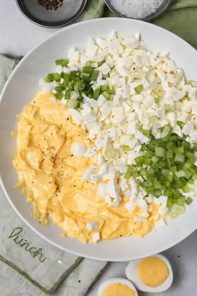 Egg salad ingredients in a bowl with mashed yolks, chopped egg whites, green onions, and celery ready to mix