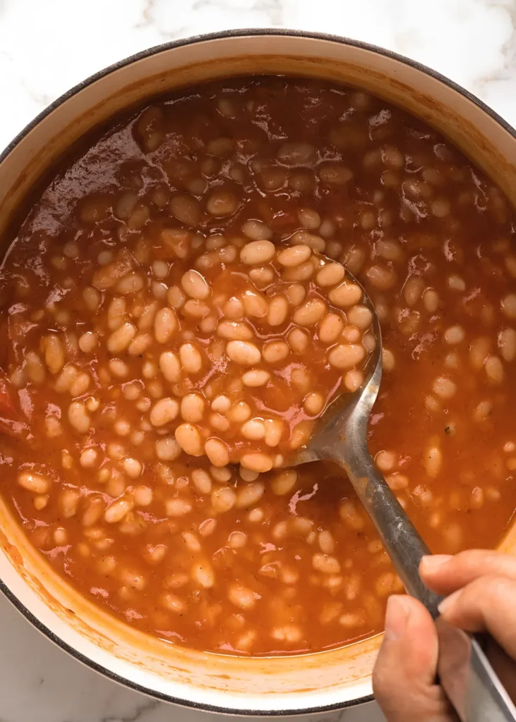 Easy baked beans in a pot with thick tomato sauce and spoon lifting tender white beans
