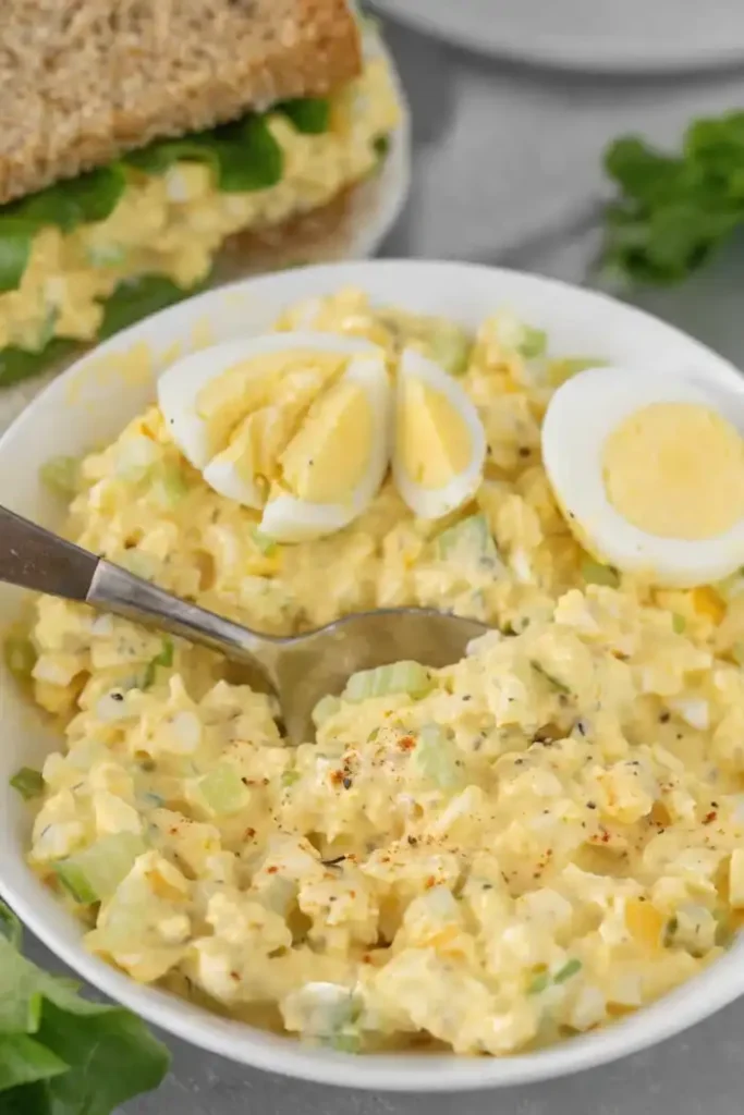 Creamy egg salad in a bowl with chopped eggs, celery, and herbs served with a spoon