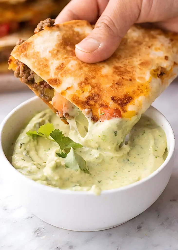 Crispy quesadilla dipped in creamy avocado sauce with melted cheese stretch