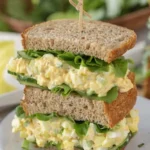 Egg salad sandwich with lettuce and cucumber on whole wheat bread stacked on a white plate